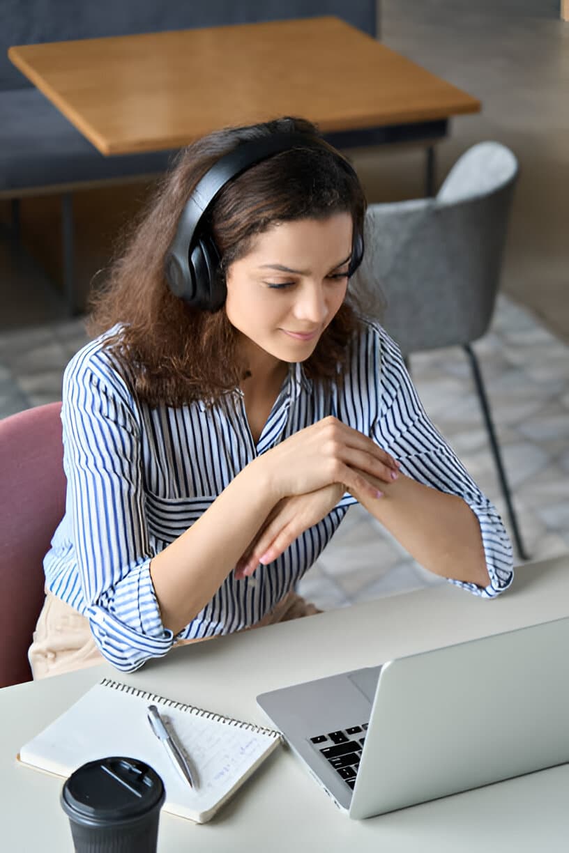 Mulher com fones de ouvido e um notebook em cima de uma mesa.